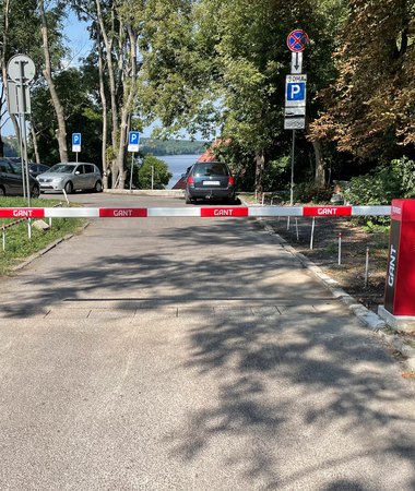 Шлагбаум на в’їзді до прибудинкової парковки, автомобілі мешканців серед зелені